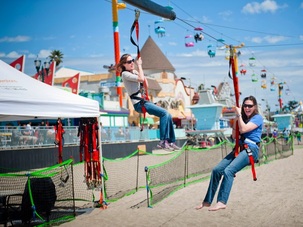 two ladies, both wearing jeans and t-shirts, having fun on a mobile zipline on a warm summers day at a fun fair